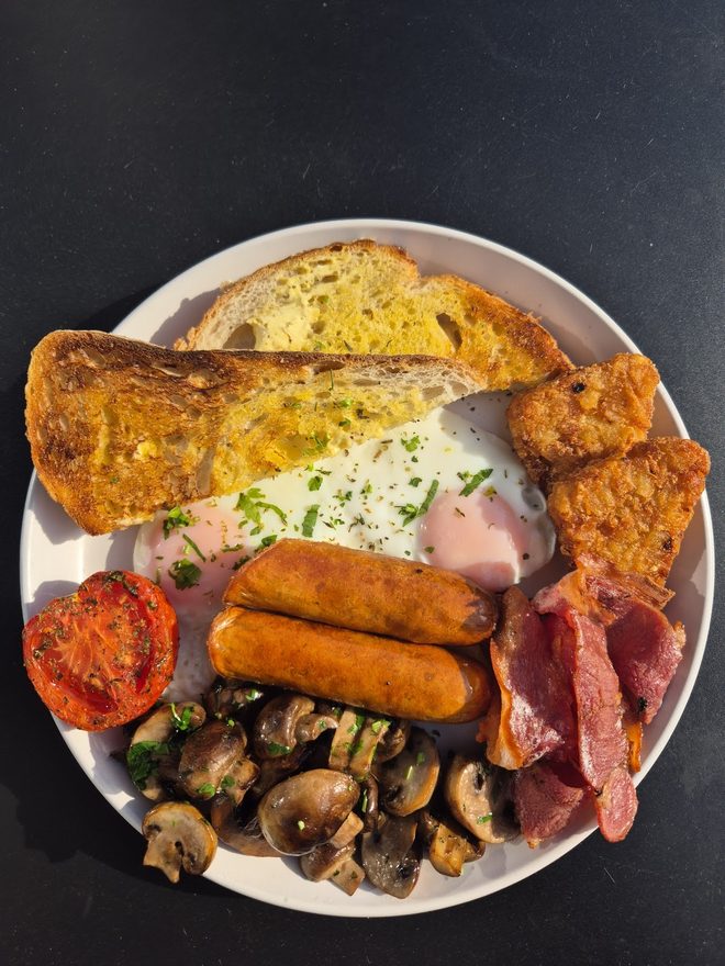 A cooked breakfast plate with egg, sausage, bacon and mushrooms