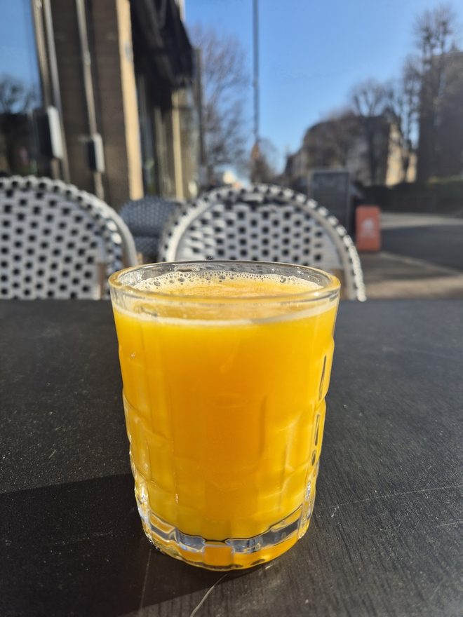 Fresh orange juice at a pavement table with Greenwich High Road behind